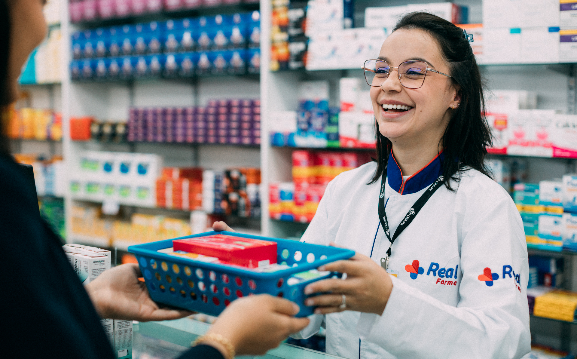 Farmacêutica da Real Farma entregando medicamentos para cliente no balcão da farmácia em Toledo.